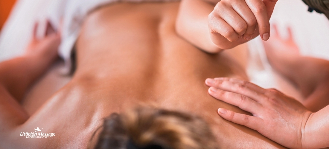 Massage therapist applying knuckle pressure to a client's upper back, highlighting the hands-on nature of sports massage treatment for muscle recovery.