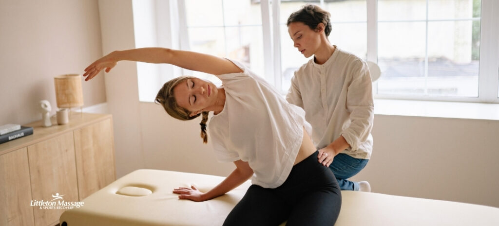 Massage therapist guiding a client through a side stretch on a treatment table to relieve work-related muscle pain and tension caused by daily occupational hazards.