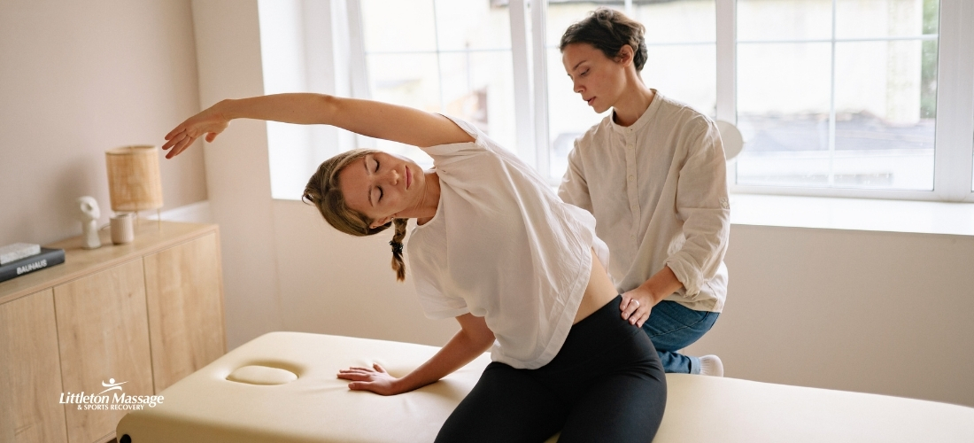 Massage therapist guiding a client through a side stretch on a treatment table to relieve work-related muscle pain and tension caused by daily occupational hazards.