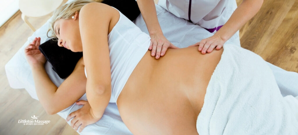 Prenatal massage therapist gently massaging a pregnant woman's lower back to relieve pregnancy discomfort.