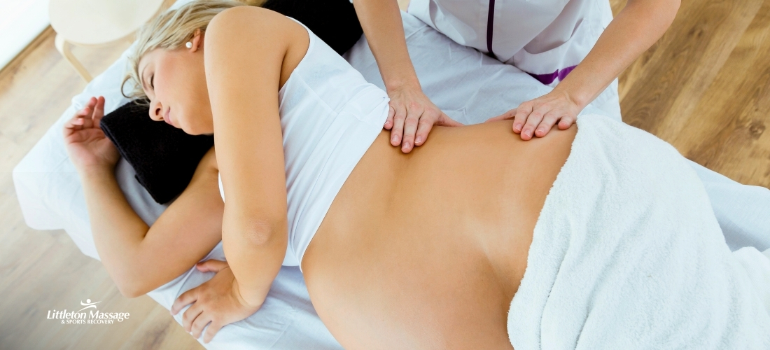Prenatal massage therapist gently massaging a pregnant woman's lower back to relieve pregnancy discomfort.