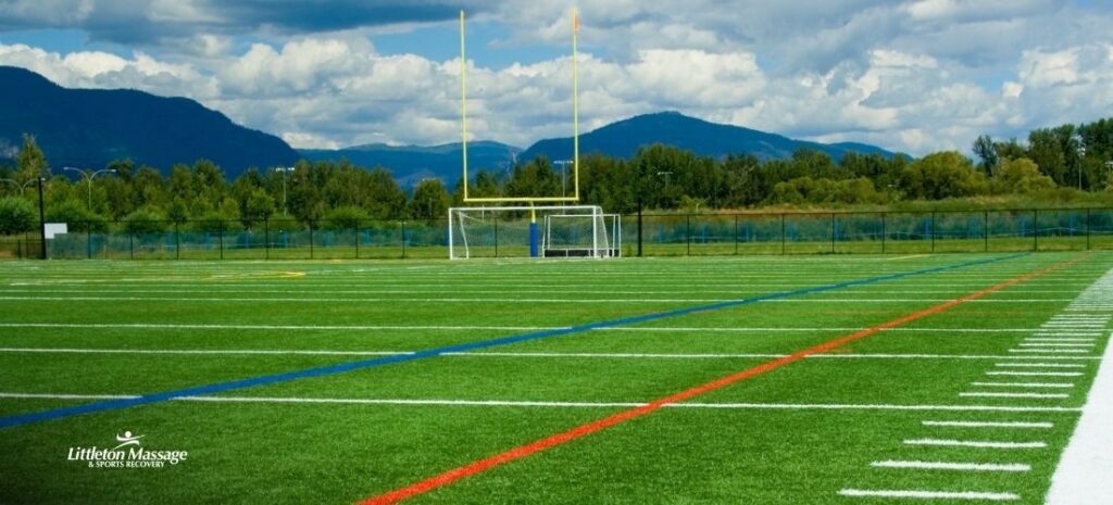 Multi-use sports field with goal posts and mountain backdrop, where teen athletes train before turning to sports massage for recovery.