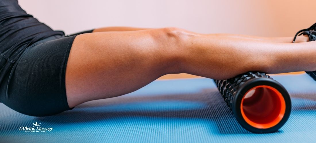 Athlete in black shorts seated on a blue mat, rolling tight calves over a spiked foam roller to ease muscle soreness and support sports recovery.